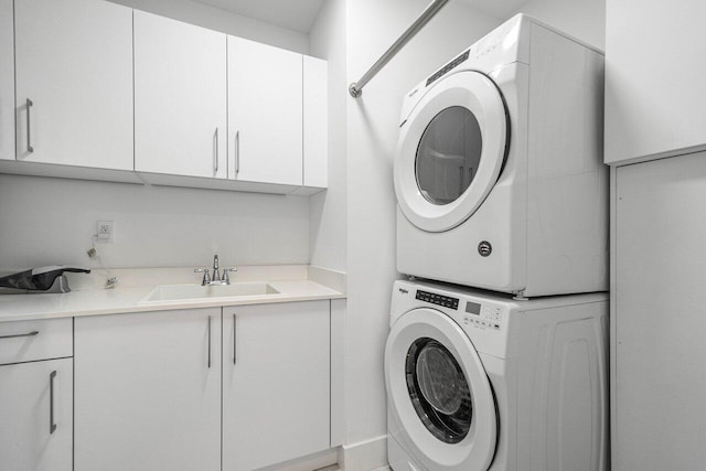 clothes washing area featuring cabinets, sink, and stacked washer and clothes dryer