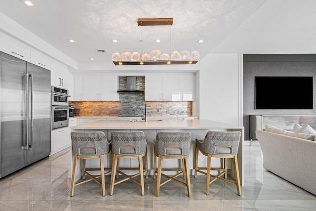 kitchen featuring white cabinets, appliances with stainless steel finishes, a kitchen breakfast bar, and wall chimney range hood