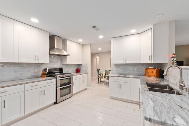 kitchen featuring sink, white cabinets, double oven range, and wall chimney range hood