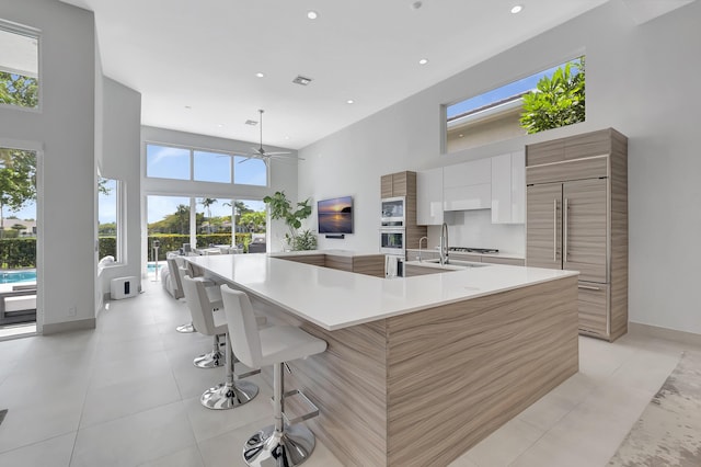 kitchen featuring white cabinets, ceiling fan, a spacious island, and a towering ceiling