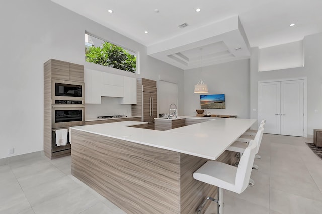 kitchen with pendant lighting, a breakfast bar, oven, a spacious island, and white cabinetry