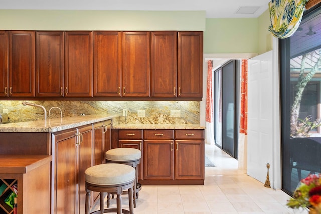 kitchen with light tile patterned flooring, light stone countertops, and backsplash