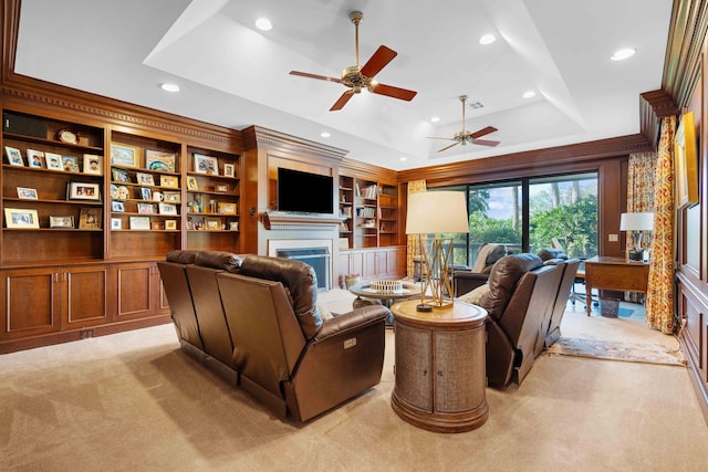 carpeted living room with a raised ceiling, ceiling fan, built in features, and ornamental molding