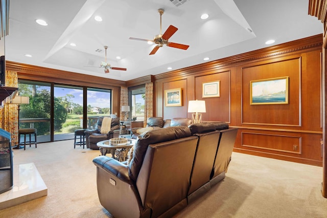 carpeted living room featuring a raised ceiling, ceiling fan, wooden walls, and crown molding