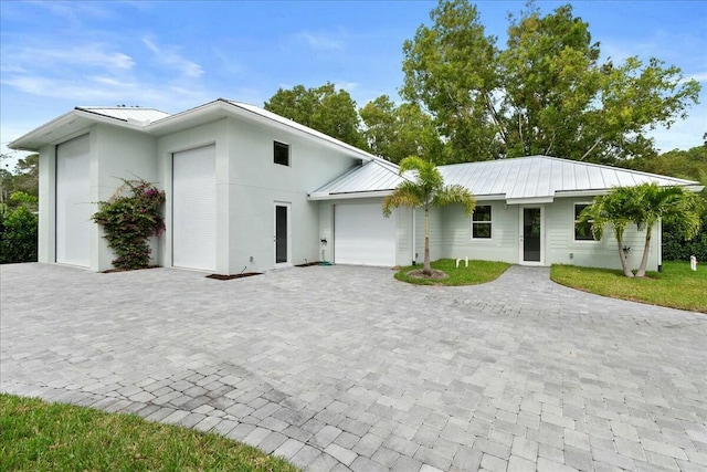 view of front facade with a garage, decorative driveway, metal roof, and stucco siding