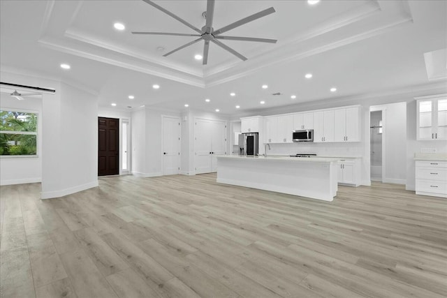 unfurnished living room featuring a ceiling fan, a raised ceiling, ornamental molding, and light wood-style flooring