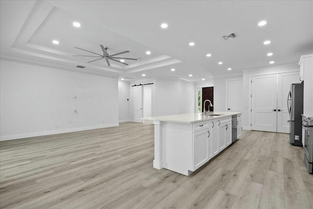 kitchen with a tray ceiling, visible vents, a barn door, appliances with stainless steel finishes, and a sink