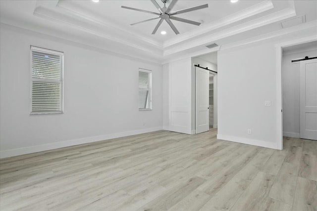 unfurnished bedroom featuring a tray ceiling, a barn door, light wood-style flooring, and visible vents