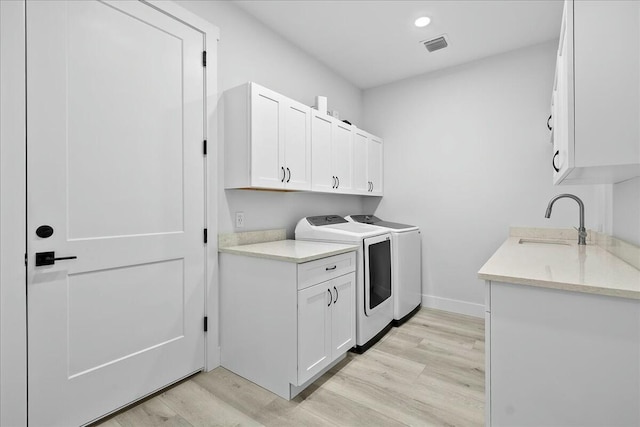 clothes washing area featuring washer and clothes dryer, light wood finished floors, visible vents, cabinet space, and a sink