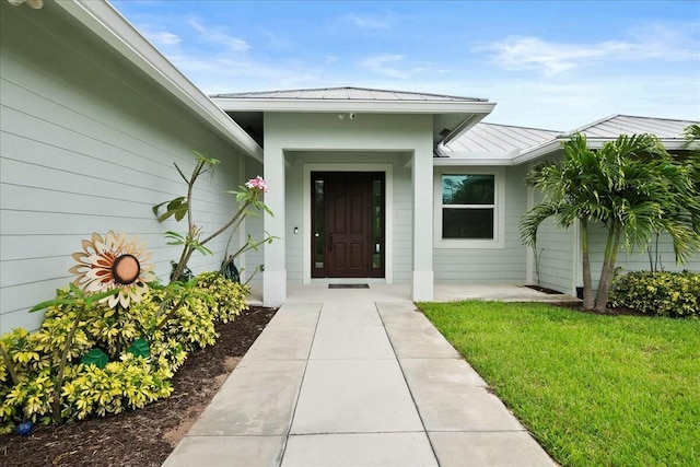 entrance to property featuring a standing seam roof, metal roof, and a yard