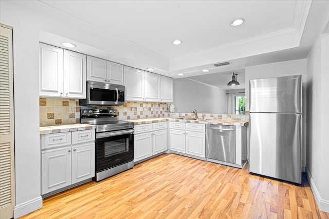 kitchen featuring light hardwood / wood-style flooring, appliances with stainless steel finishes, decorative backsplash, white cabinets, and ornamental molding