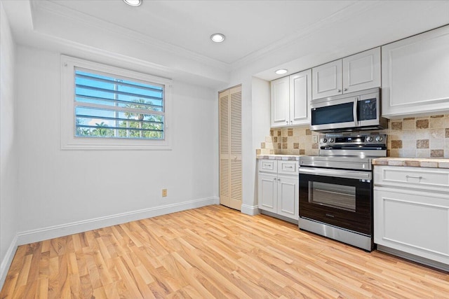 kitchen with backsplash, white cabinets, stainless steel appliances, and light hardwood / wood-style flooring