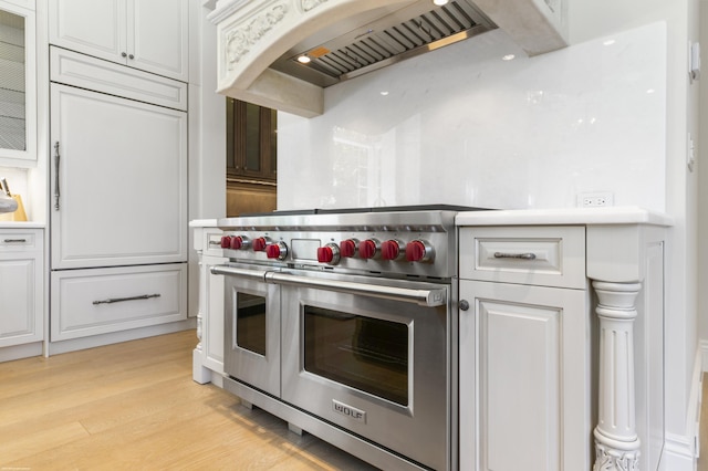 kitchen with white cabinets, wall chimney exhaust hood, double oven range, and light hardwood / wood-style flooring