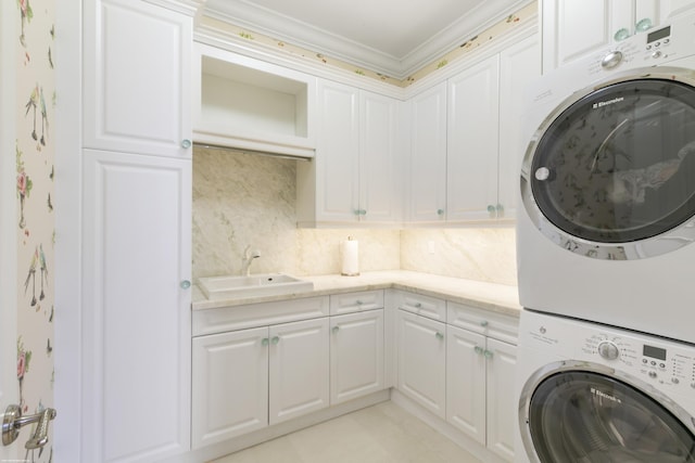 laundry area featuring crown molding, cabinets, sink, and stacked washer and clothes dryer