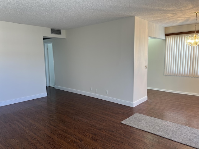 spare room featuring a textured ceiling, dark hardwood / wood-style floors, and an inviting chandelier