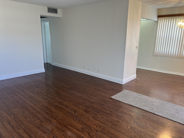 spare room featuring dark hardwood / wood-style flooring, a textured ceiling, and a notable chandelier