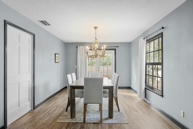 dining space with light hardwood / wood-style flooring, a textured ceiling, and an inviting chandelier