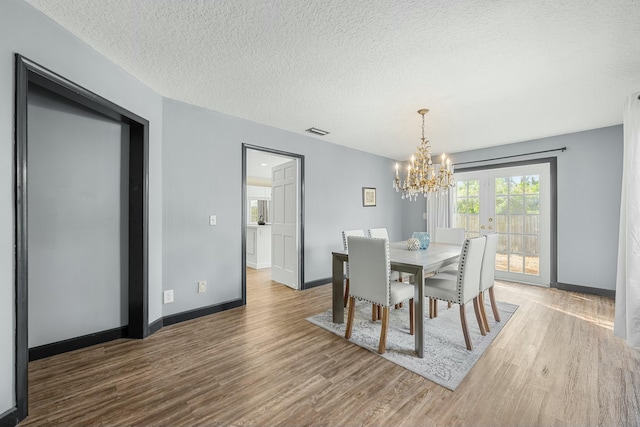 dining space with hardwood / wood-style floors, a textured ceiling, and an inviting chandelier