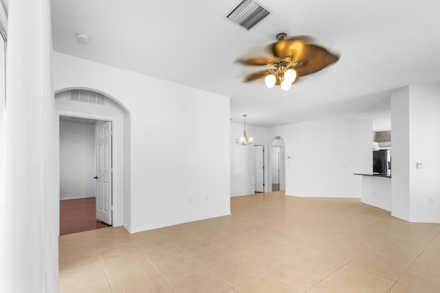 tiled empty room with ceiling fan with notable chandelier