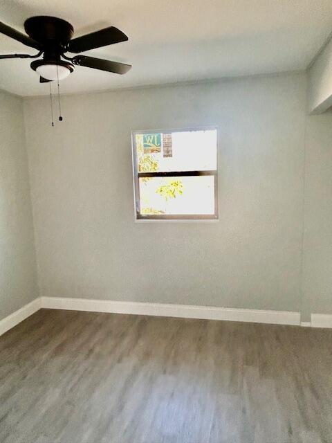 spare room with baseboards, dark wood-style flooring, and ceiling fan