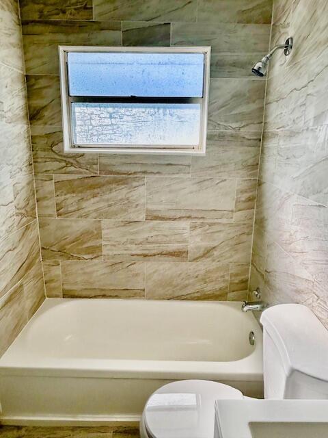 bathroom with tiled shower / bath combo and toilet