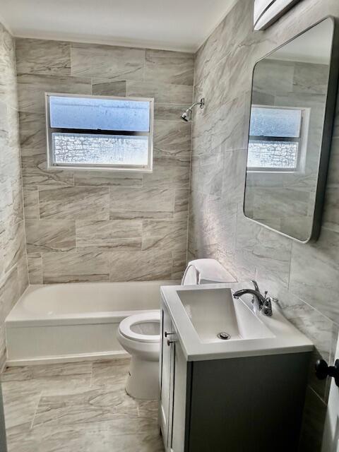 full bath with vanity, bathing tub / shower combination, toilet, and tile walls
