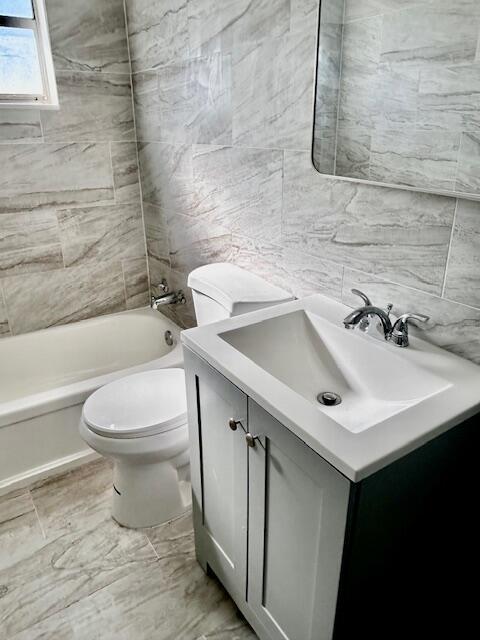 full bath with toilet, tile walls, tub / shower combination, and vanity