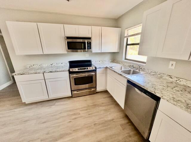 kitchen with white cabinets, appliances with stainless steel finishes, a sink, and light wood-type flooring