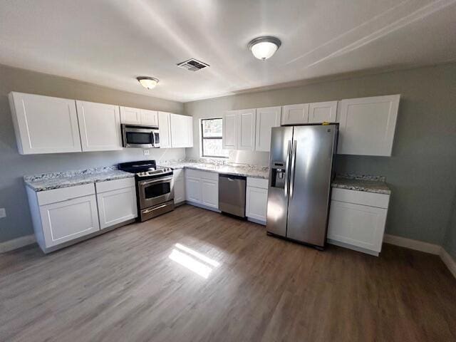 kitchen with dark hardwood / wood-style floors, light stone counters, white cabinetry, and stainless steel appliances