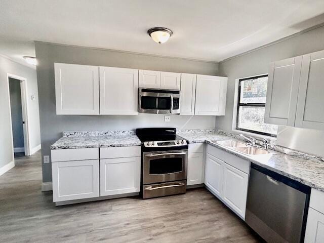 kitchen with light stone countertops, stainless steel appliances, sink, light hardwood / wood-style floors, and white cabinetry