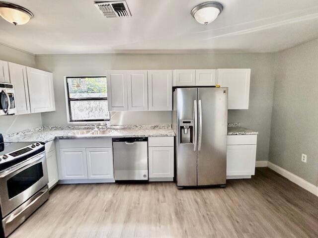 kitchen featuring appliances with stainless steel finishes, light wood-type flooring, light stone counters, sink, and white cabinets