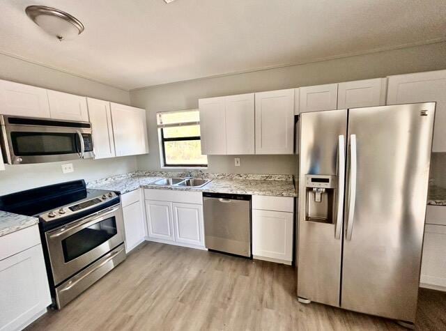 kitchen with a sink, light wood-style flooring, appliances with stainless steel finishes, and white cabinets