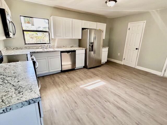 kitchen with white cabinets, light stone counters, light wood-type flooring, and stainless steel appliances