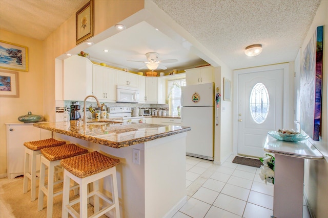 kitchen featuring sink, white cabinets, white appliances, light tile patterned flooring, and kitchen peninsula