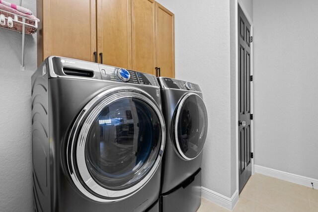 clothes washing area with cabinets, independent washer and dryer, and light tile patterned floors