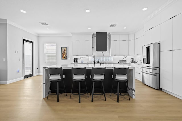 kitchen with white cabinetry, high end refrigerator, light hardwood / wood-style floors, a kitchen island with sink, and a breakfast bar