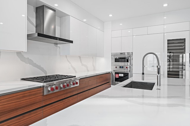 kitchen featuring a sink, wall chimney range hood, stainless steel appliances, white cabinetry, and modern cabinets