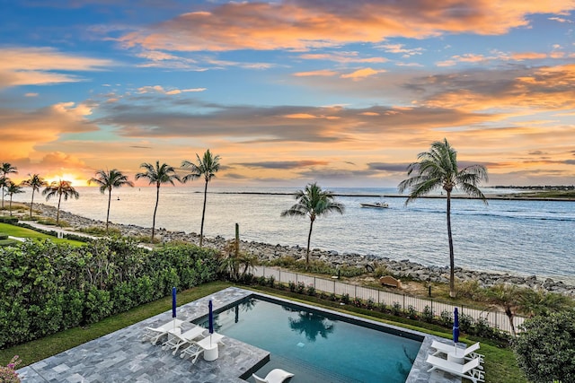 pool at dusk featuring a patio area and a water view