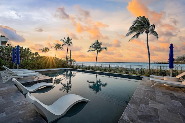 pool at dusk with a water view and a patio area