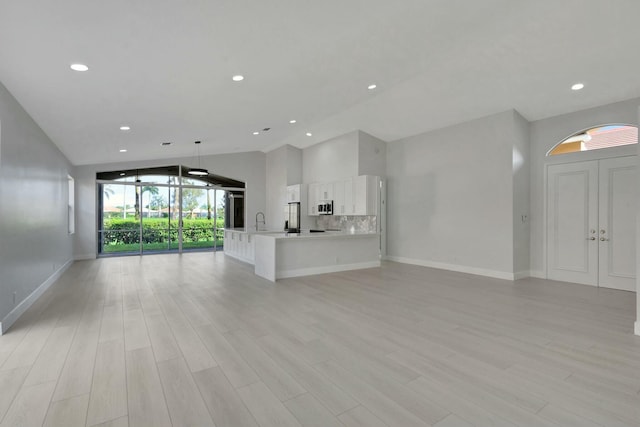 unfurnished living room with light wood-type flooring, sink, and vaulted ceiling