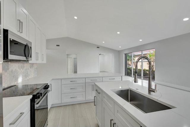 kitchen with sink, white cabinetry, stainless steel appliances, and vaulted ceiling