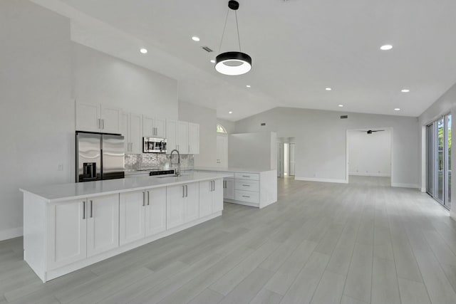 kitchen featuring appliances with stainless steel finishes, tasteful backsplash, a large island with sink, white cabinetry, and lofted ceiling