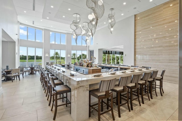 kitchen featuring kitchen peninsula, a kitchen bar, pendant lighting, a high ceiling, and light tile patterned flooring