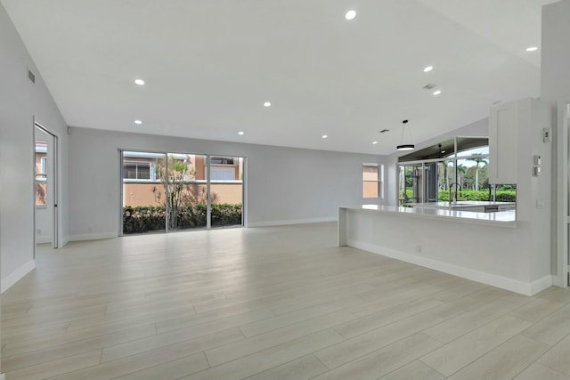 unfurnished living room featuring light hardwood / wood-style flooring, a healthy amount of sunlight, sink, and vaulted ceiling