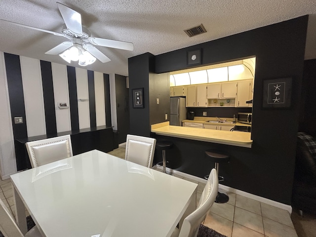 tiled dining room with ceiling fan, sink, and a textured ceiling