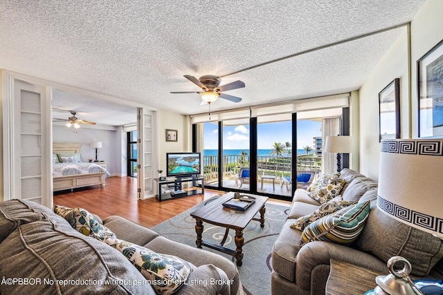 living room with wood-type flooring, a textured ceiling, expansive windows, and ceiling fan