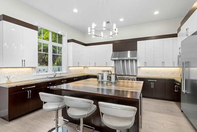 kitchen featuring pendant lighting, sink, wall chimney range hood, wooden counters, and a kitchen island