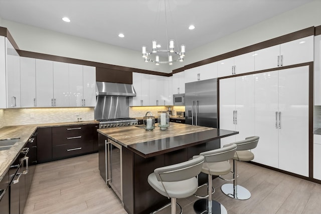 kitchen with light hardwood / wood-style flooring, a center island, built in appliances, dark brown cabinetry, and wall chimney exhaust hood