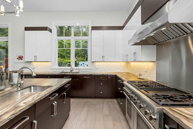 kitchen featuring sink, double oven range, range hood, white cabinets, and decorative light fixtures