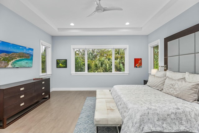 bedroom with a tray ceiling, light hardwood / wood-style floors, and ceiling fan